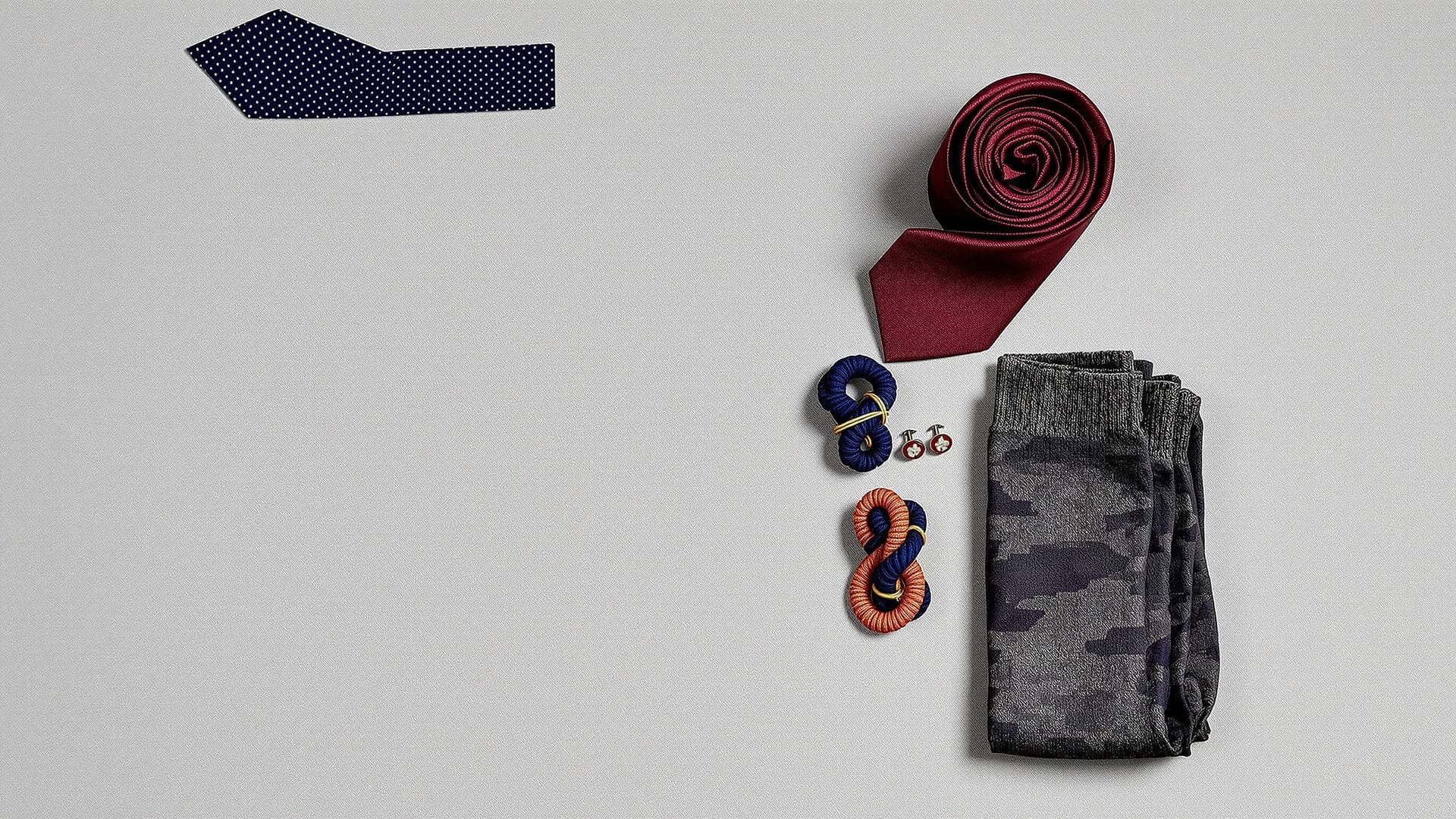 Woven silk ties, mother-of-pearl cufflinks, silk knots and folded cotton socks arranged on linen
